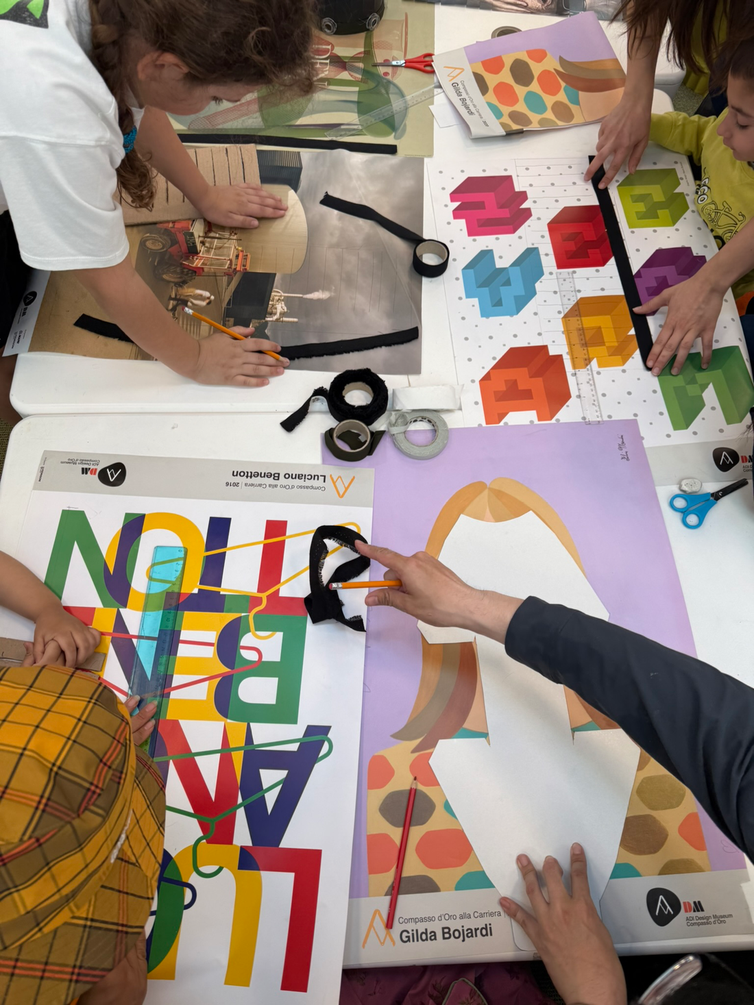 Bambini al tavolo del laboratorio ritagliano manifesti del Compasso d'Oro